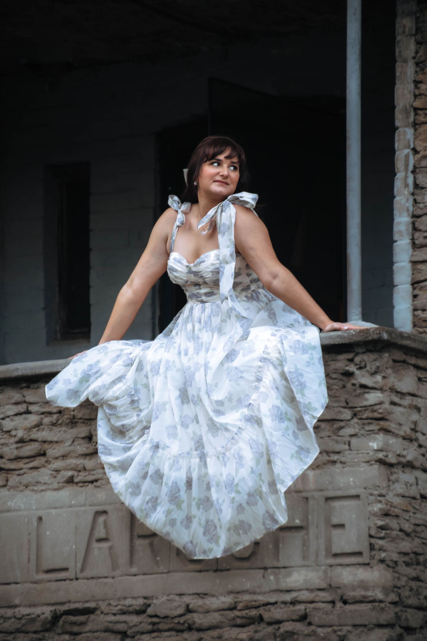 White floral dress photoshoot with playful poses on stone ledge.
