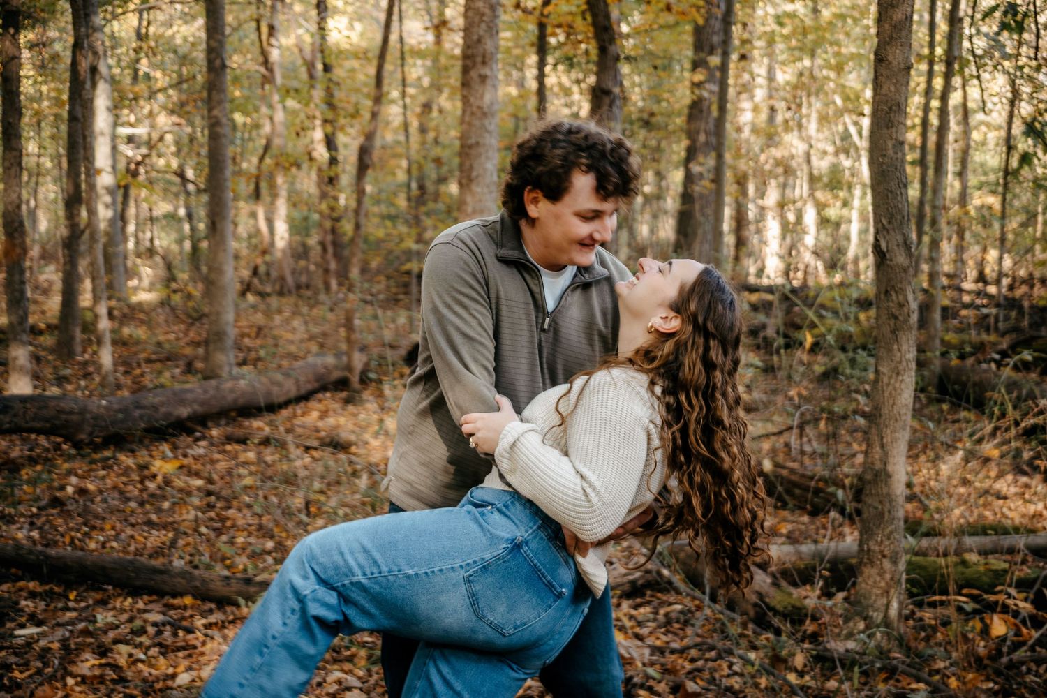 Romantic woodland photoshoot with couple in casual attire among trees.