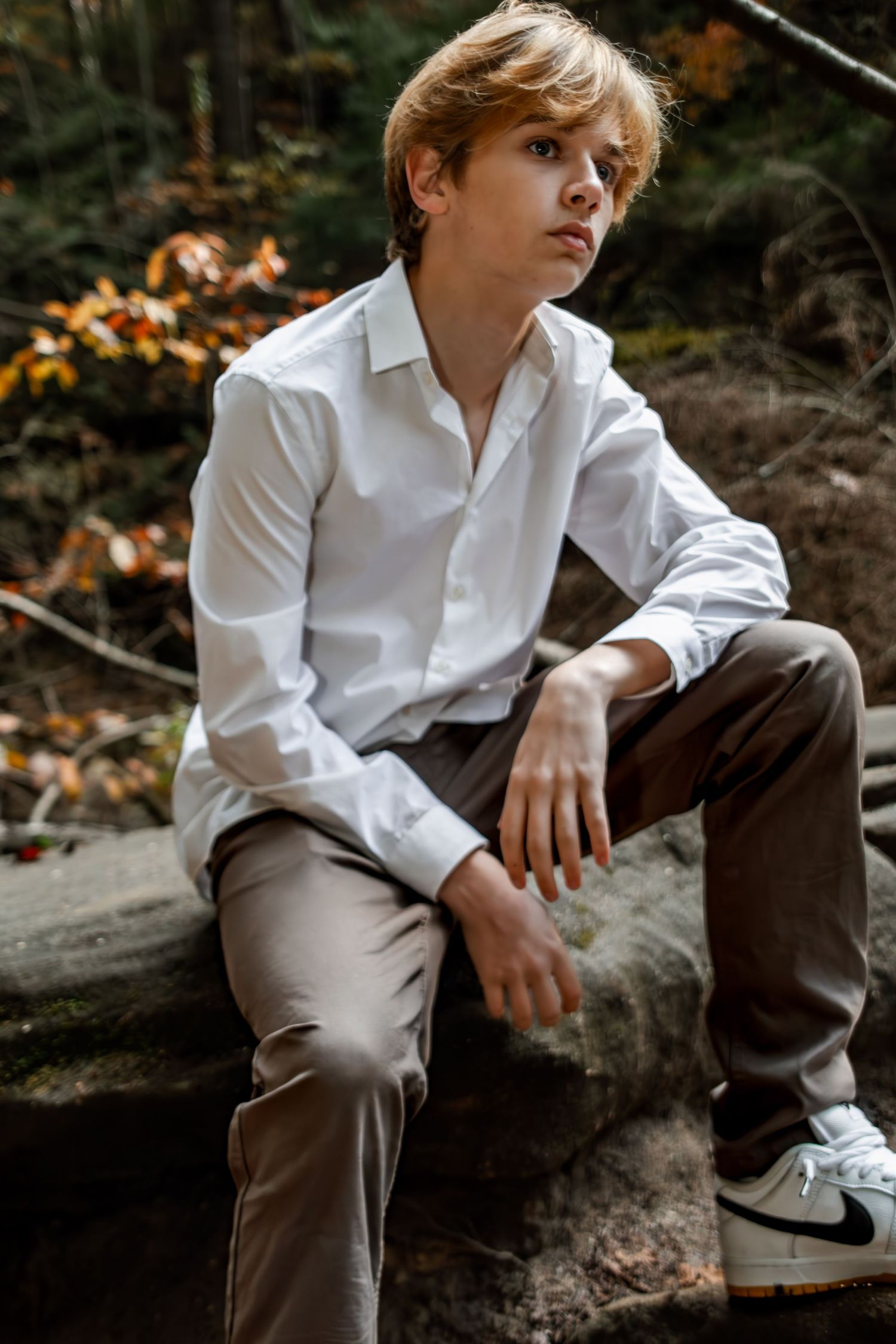 A person in white shirt and brown pants sits contemplatively on natural rock formations.