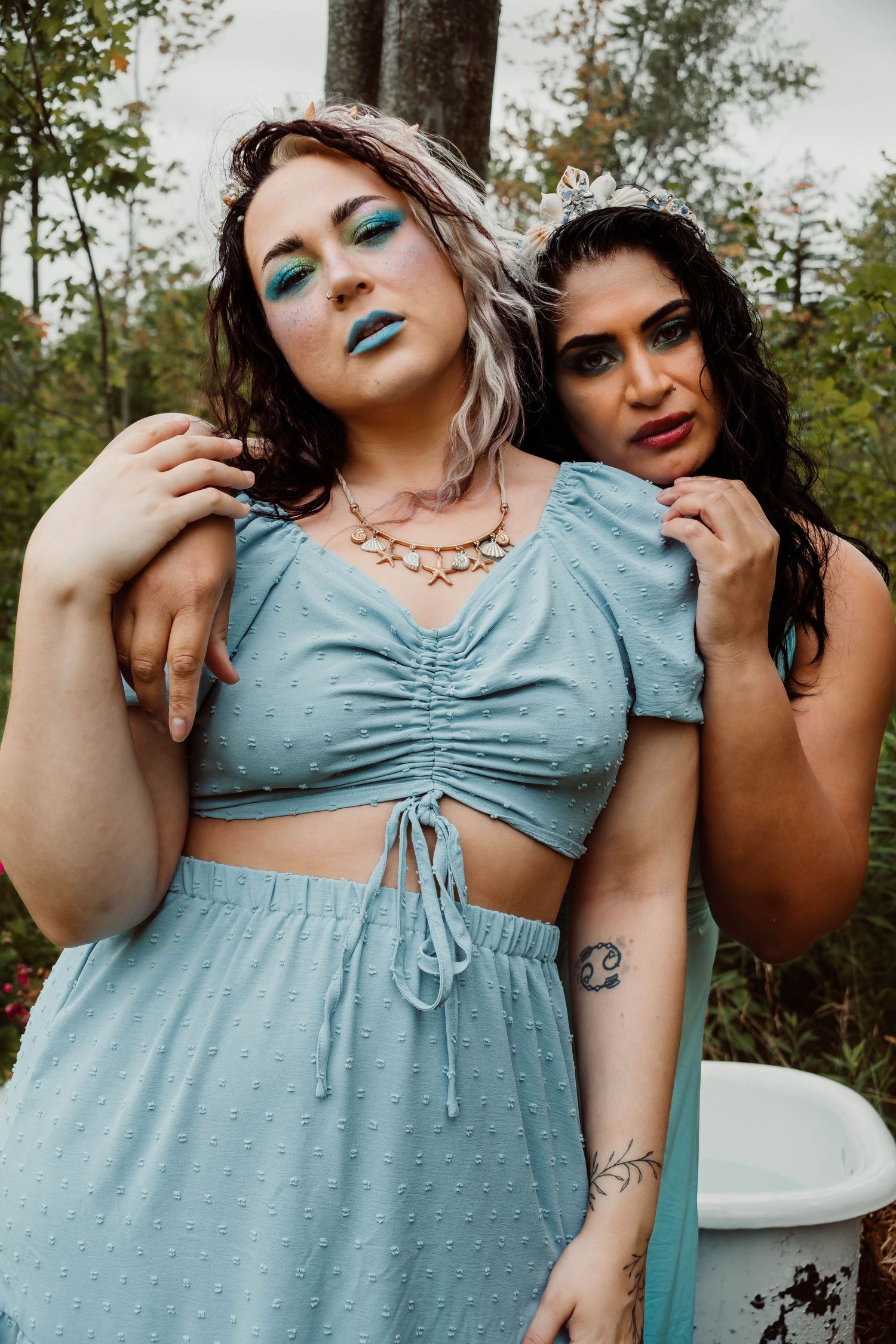 Two models in a romantic outdoor photoshoot wearing blue and black outfits against a natural backdrop.