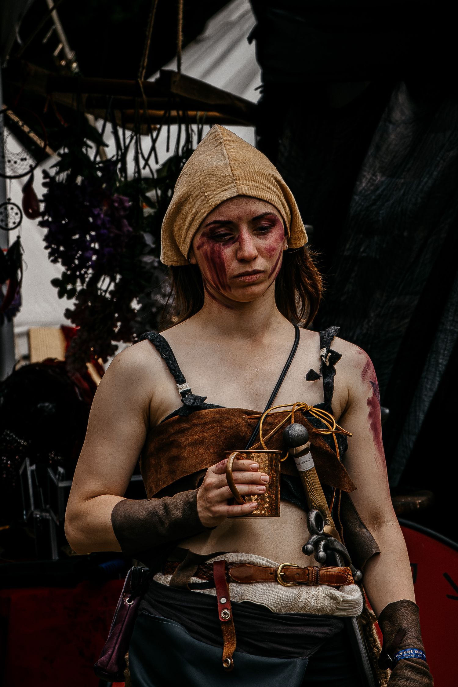 Woman in medieval warrior costume with fake wounds, holding a copper mug at a Renaissance fair.