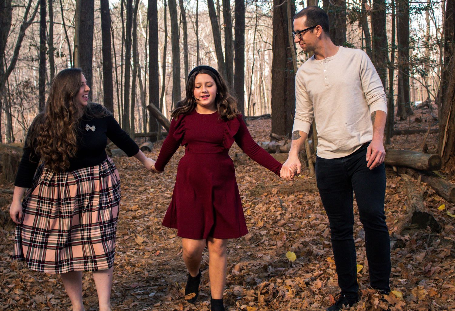 Family walking together through autumn forest with fallen leaves covering the ground.