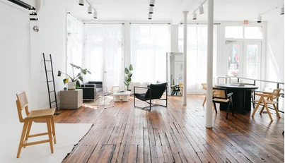 Modern open concept office interior with white walls, hardwood floors, and natural light streaming through large windows.
