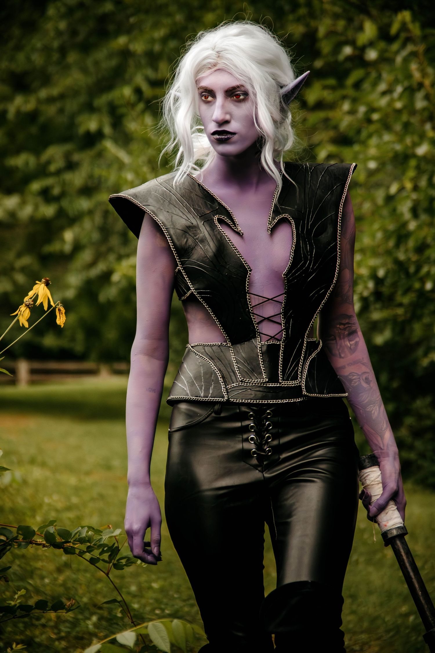 Dark fantasy cosplay featuring a figure in black leather with white hair and dramatic makeup in an outdoor setting.