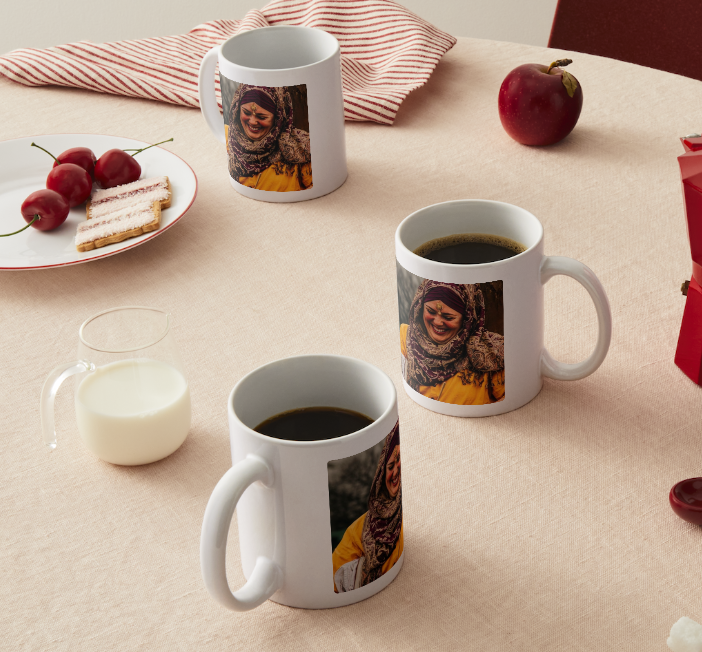 A white coffee mug sits on a table with a red and white striped cloth and scattered red cherries.