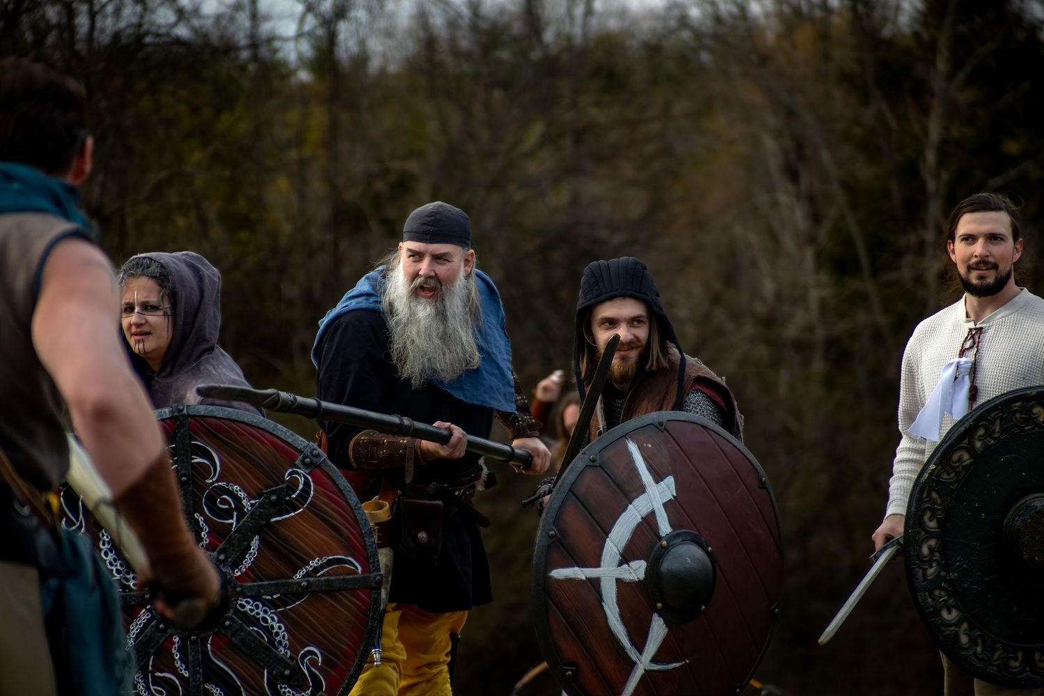 Medieval reenactors with ornate shields and period costumes gather outdoors during a historical demonstration.