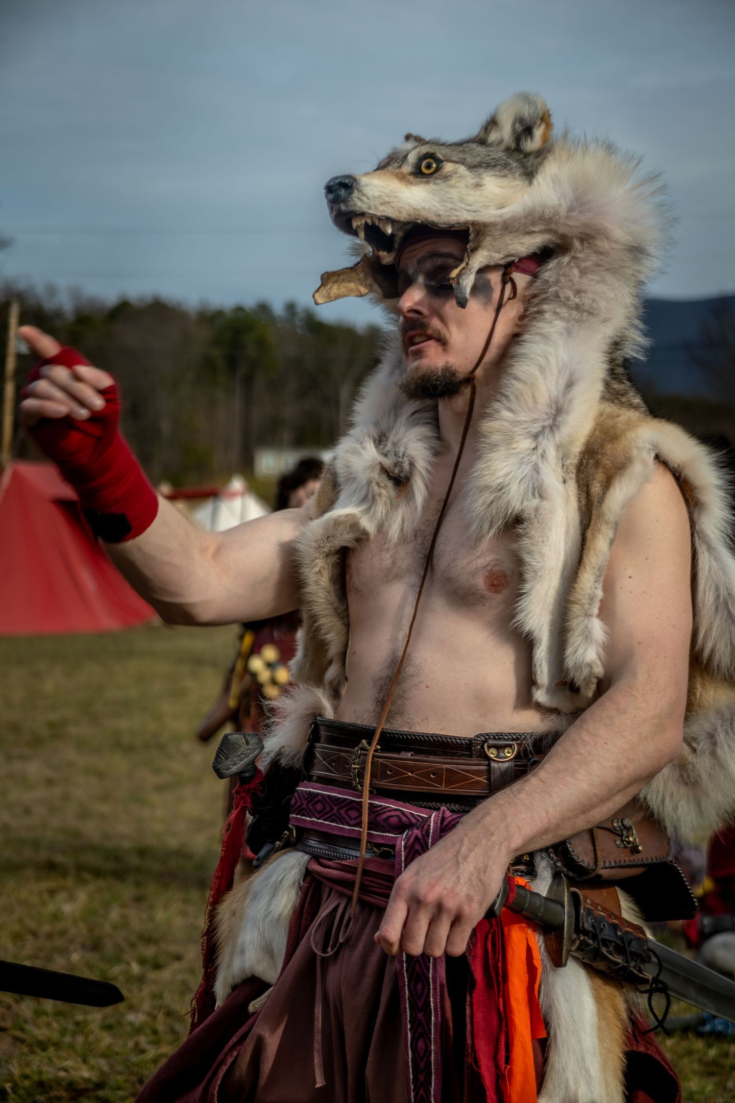 A person in historical reenactment costume wearing wolf fur and leather garments stands in an outdoor field.