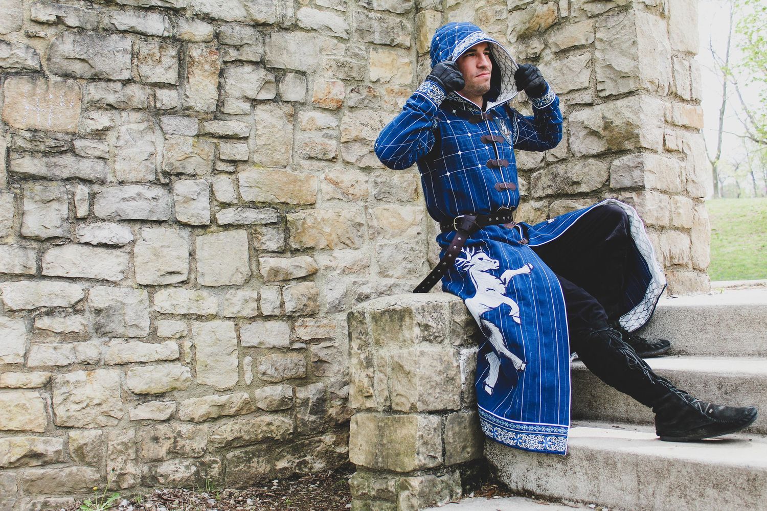 A person in a blue patterned sweater sits on a stone ledge near an old brick wall.