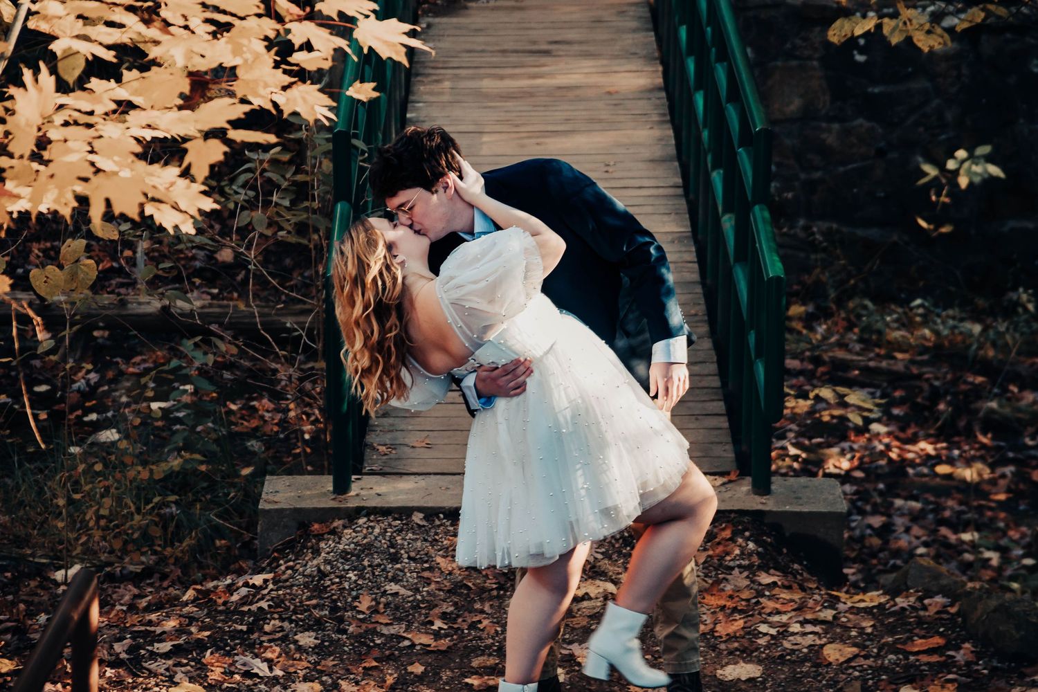 Couple poses playfully on wooden boardwalk surrounded by fall foliage.