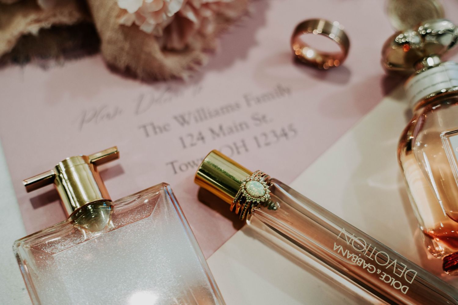 Elegant perfume bottles and wedding rings arranged with invitation details.