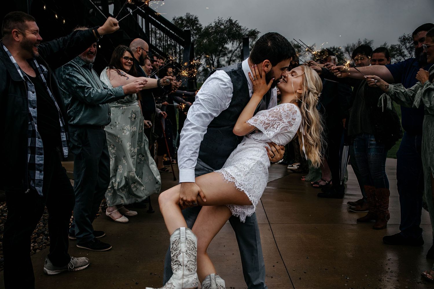 Couples dance together at a lively wedding reception on a dark dance floor surrounded by other guests.