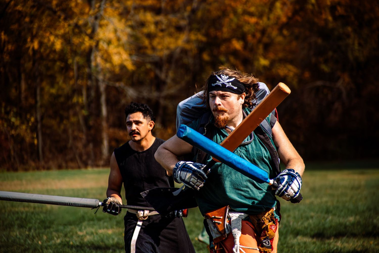 Baseball players practicing batting drills on a sunny autumn field with golden trees in the background.