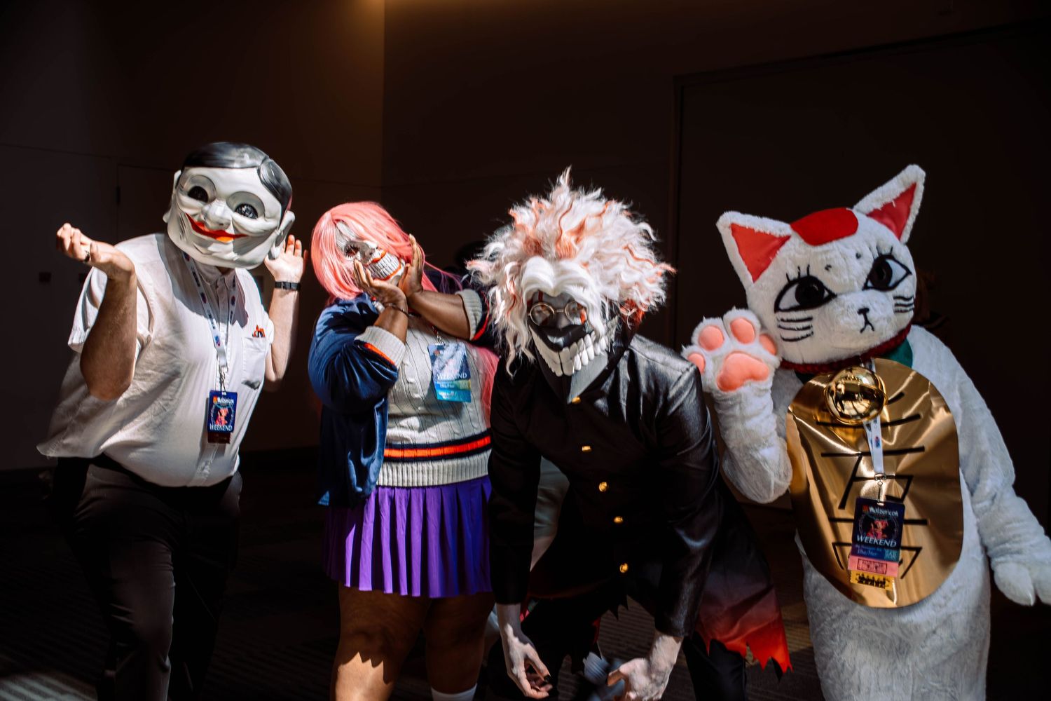 Four cosplayers in anime cat masks and costumes pose together at a convention event.