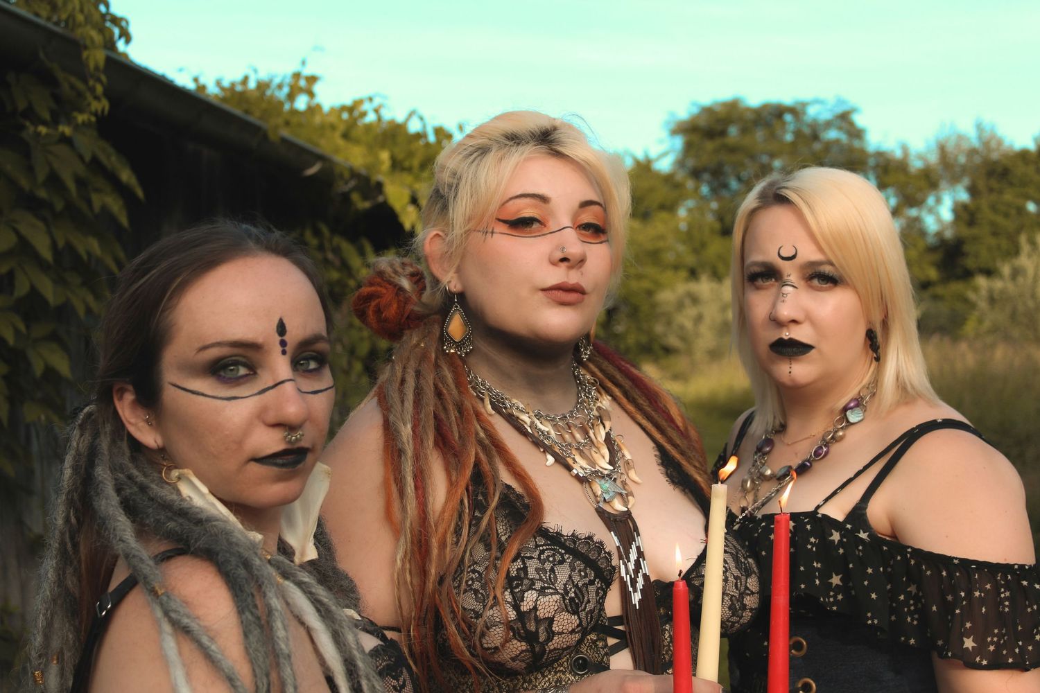 Group of people in gothic-inspired dark makeup and attire pose together outdoors during a photoshoot.