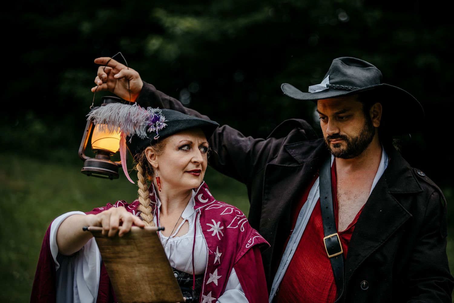 Two people in pirate costumes holding a lantern and barrel outdoors in a forest setting.