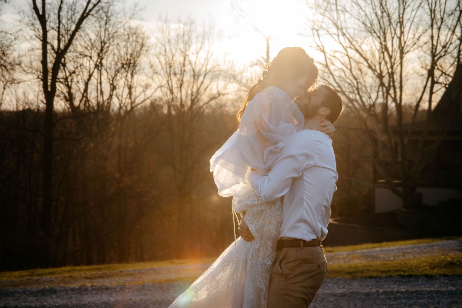 Romantic silhouette of couple embracing at sunset among bare trees.