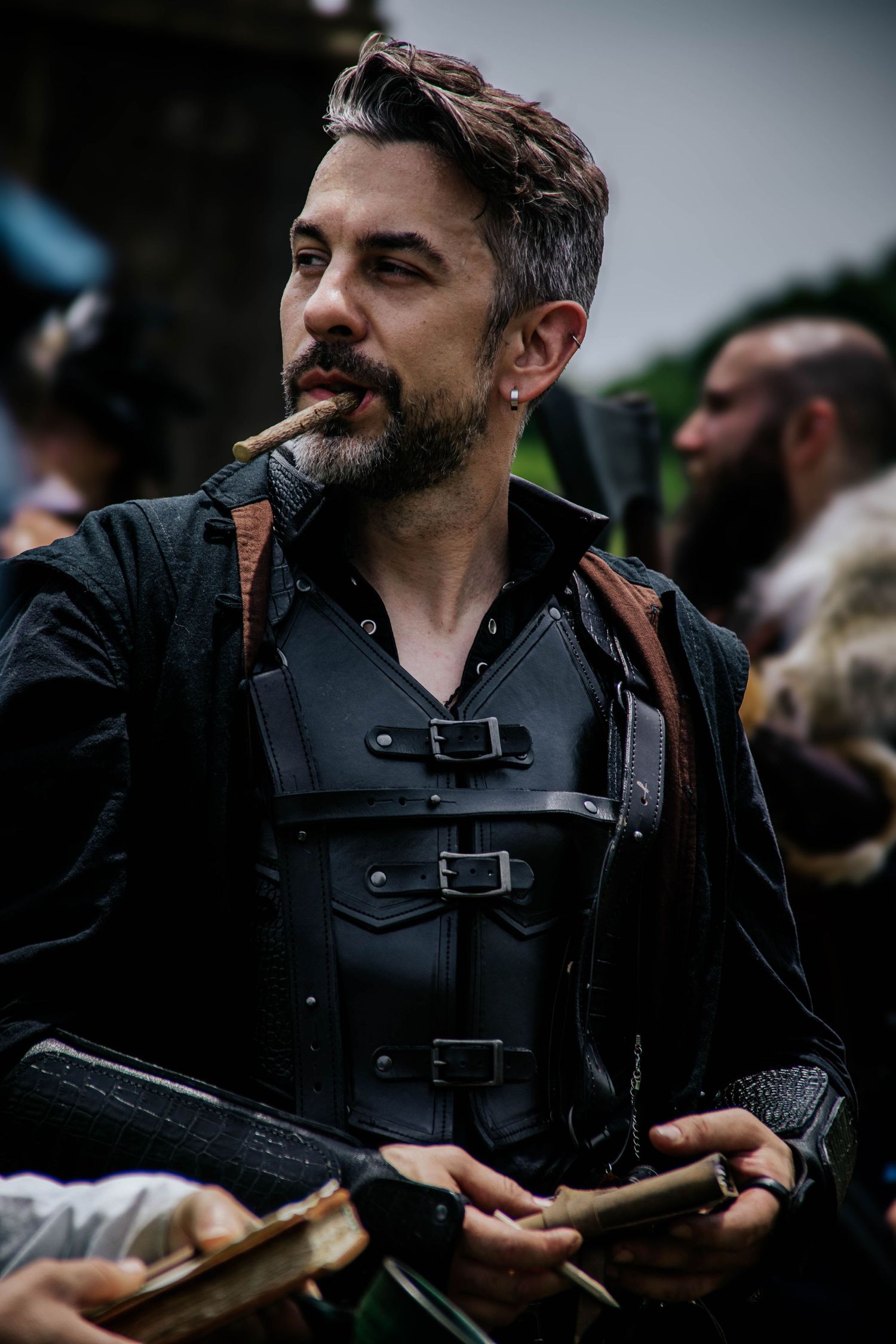 A reenactor in tactical gear and dark clothing holds equipment during an event.