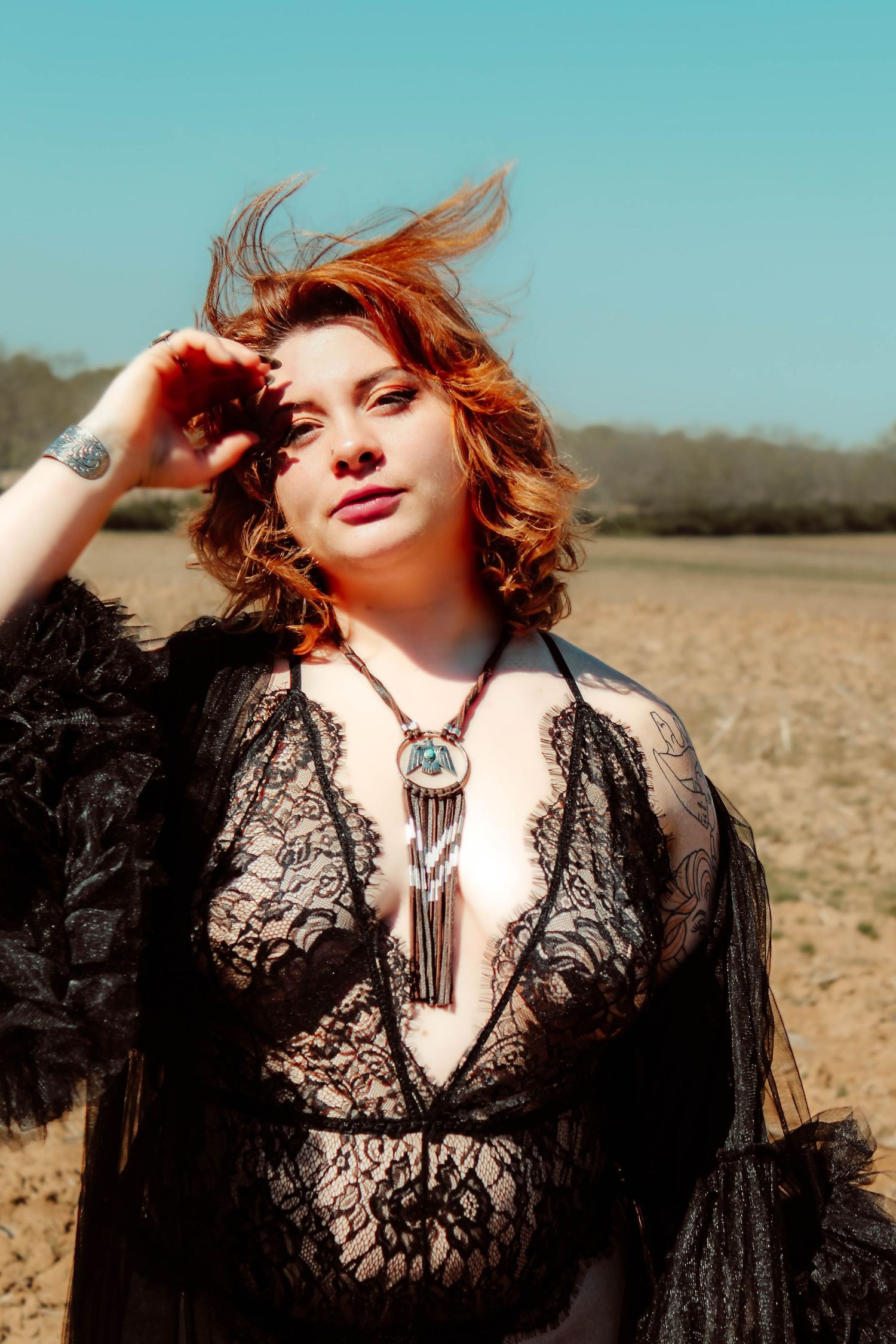 Outdoor portrait in black lace dress with statement necklace against turquoise sky.