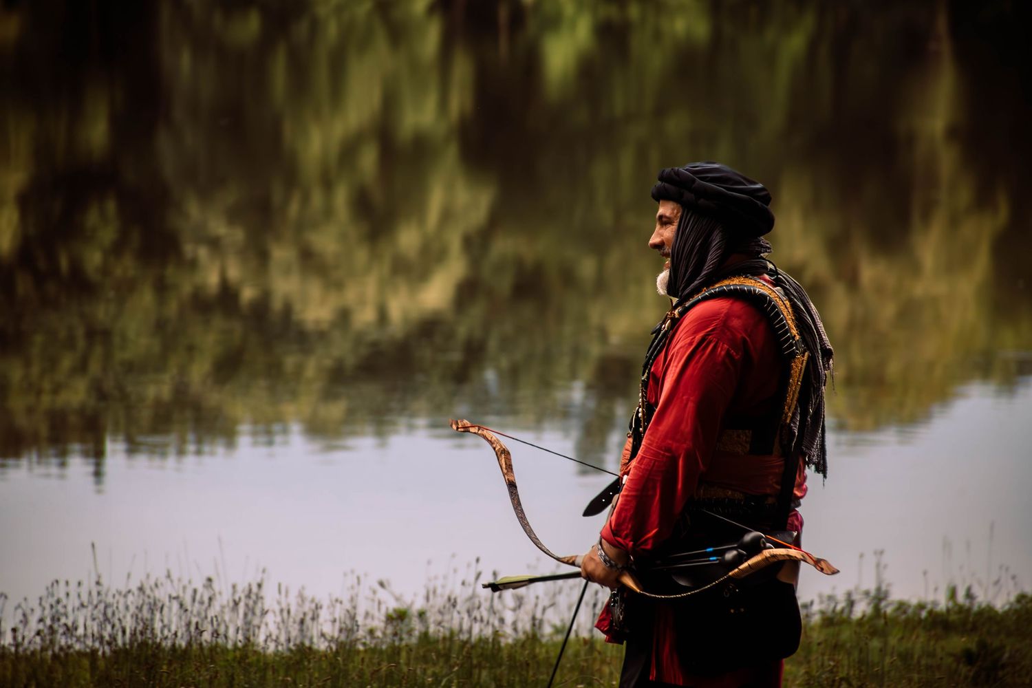 Silhouetted figures by a lake during golden hour wearing outdoor gear.