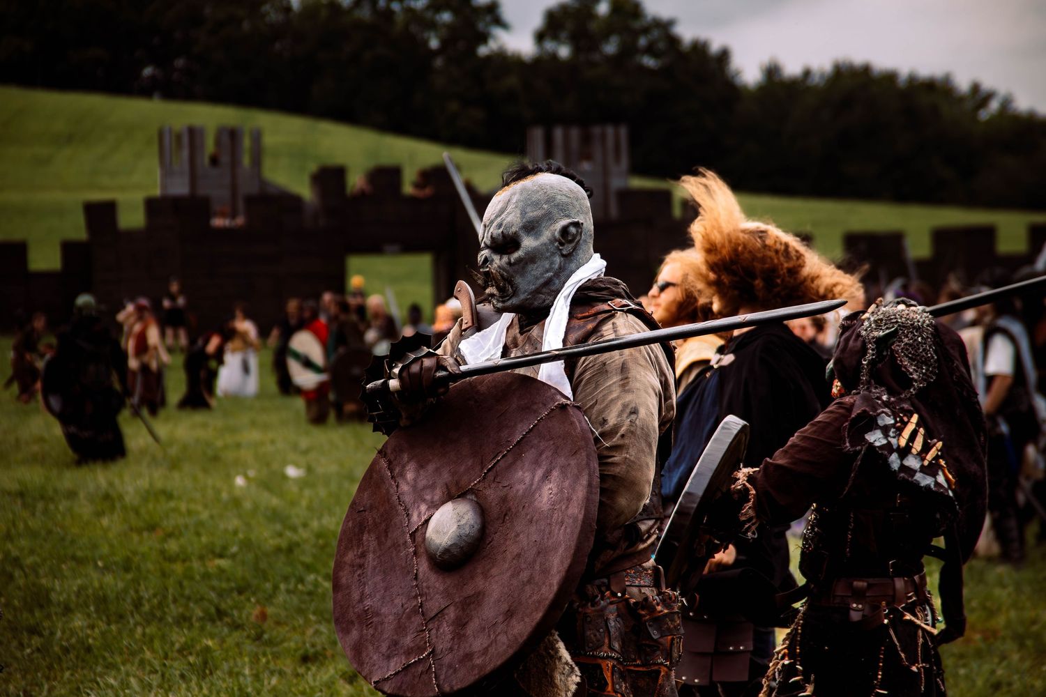 Medieval reenactors engage in combat with shields and weapons at an outdoor festival gathering.
