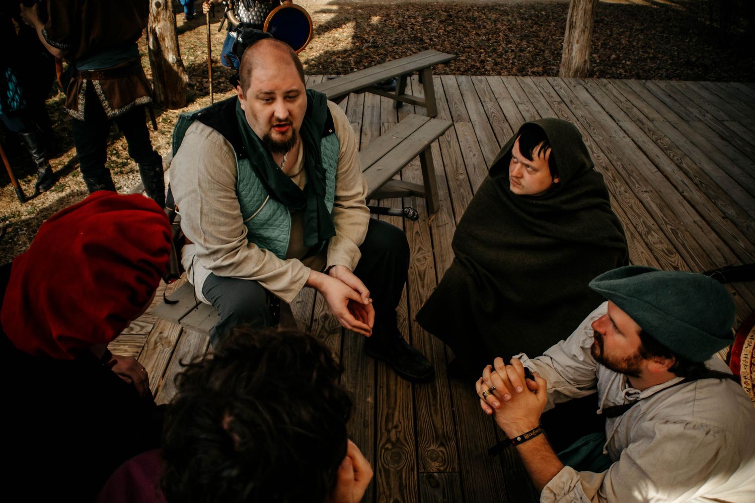 A group of people gather around a wooden table outdoors during a casual social gathering.