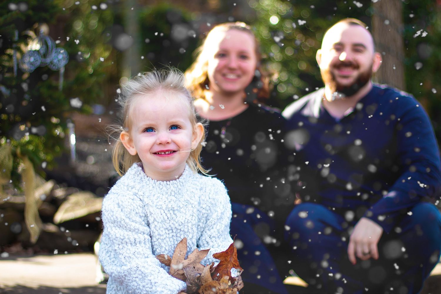 A family enjoying a playful moment outdoors with falling leaves during an autumn photo session.