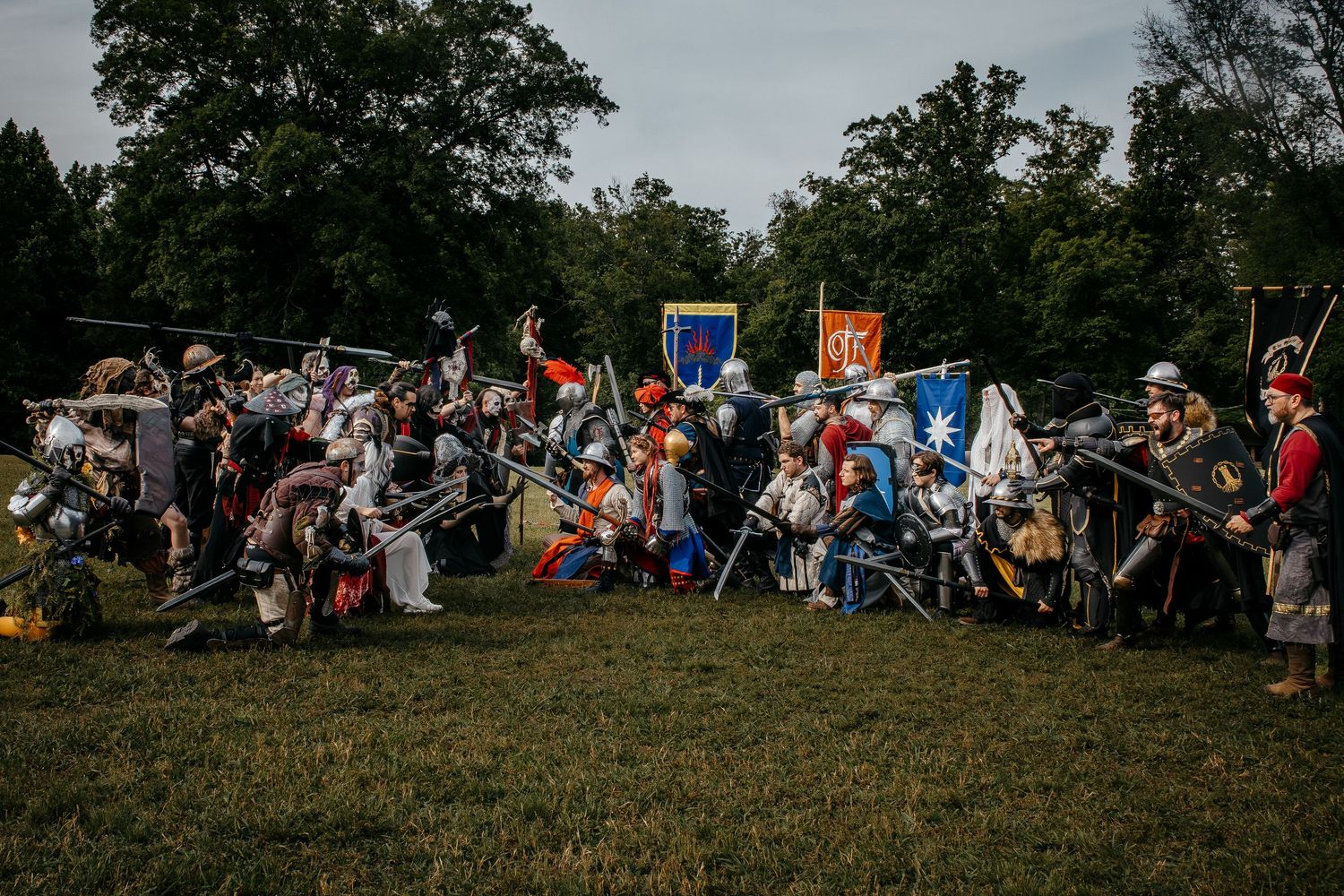 Medieval battle reenactment with armored knights wielding spears and shields on a grassy field at dusk.