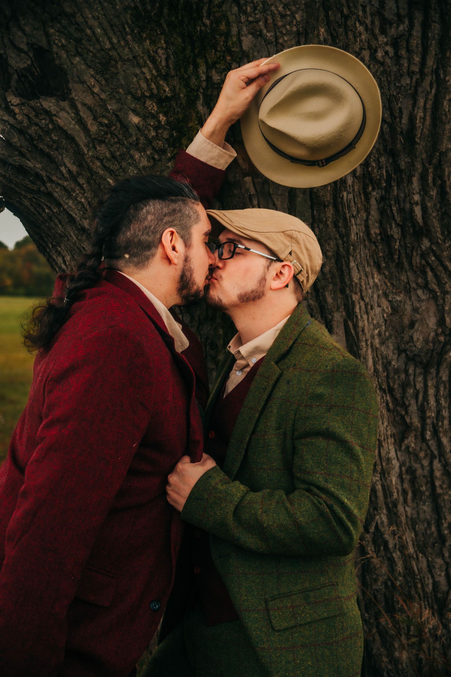 Intimate moment shared between couple wearing hats against tree backdrop.