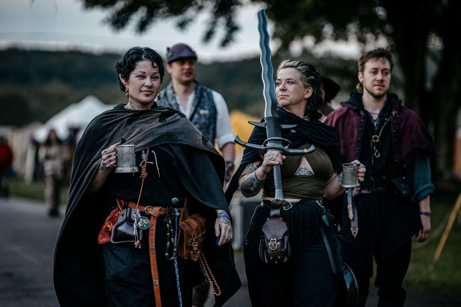 Medieval costumed performers walk at a Renaissance faire, with a woman wielding a sword leading the group.