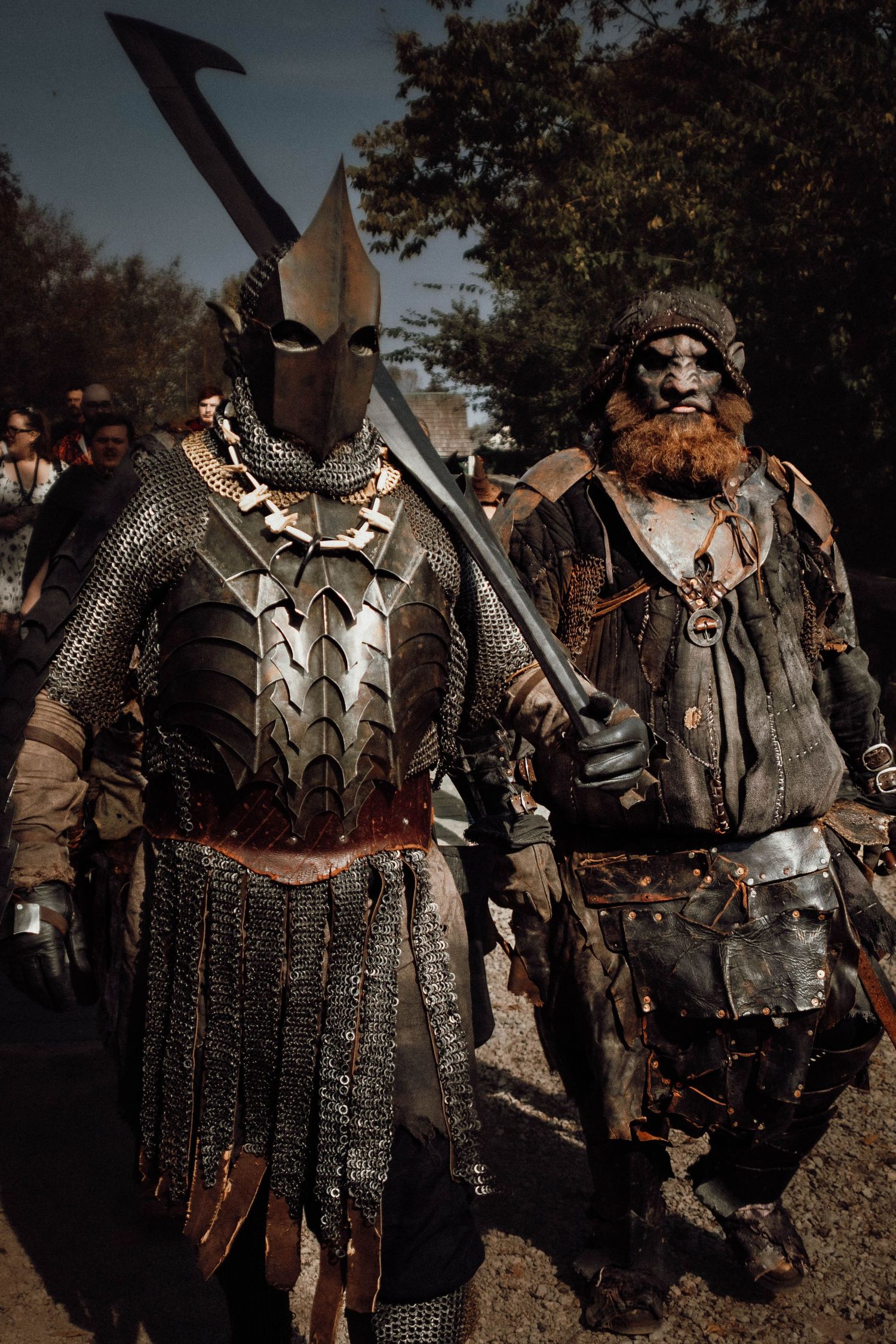 Medieval warriors in chainmail armor and leather garments stand together displaying ornate battle gear at a historical reenactment.