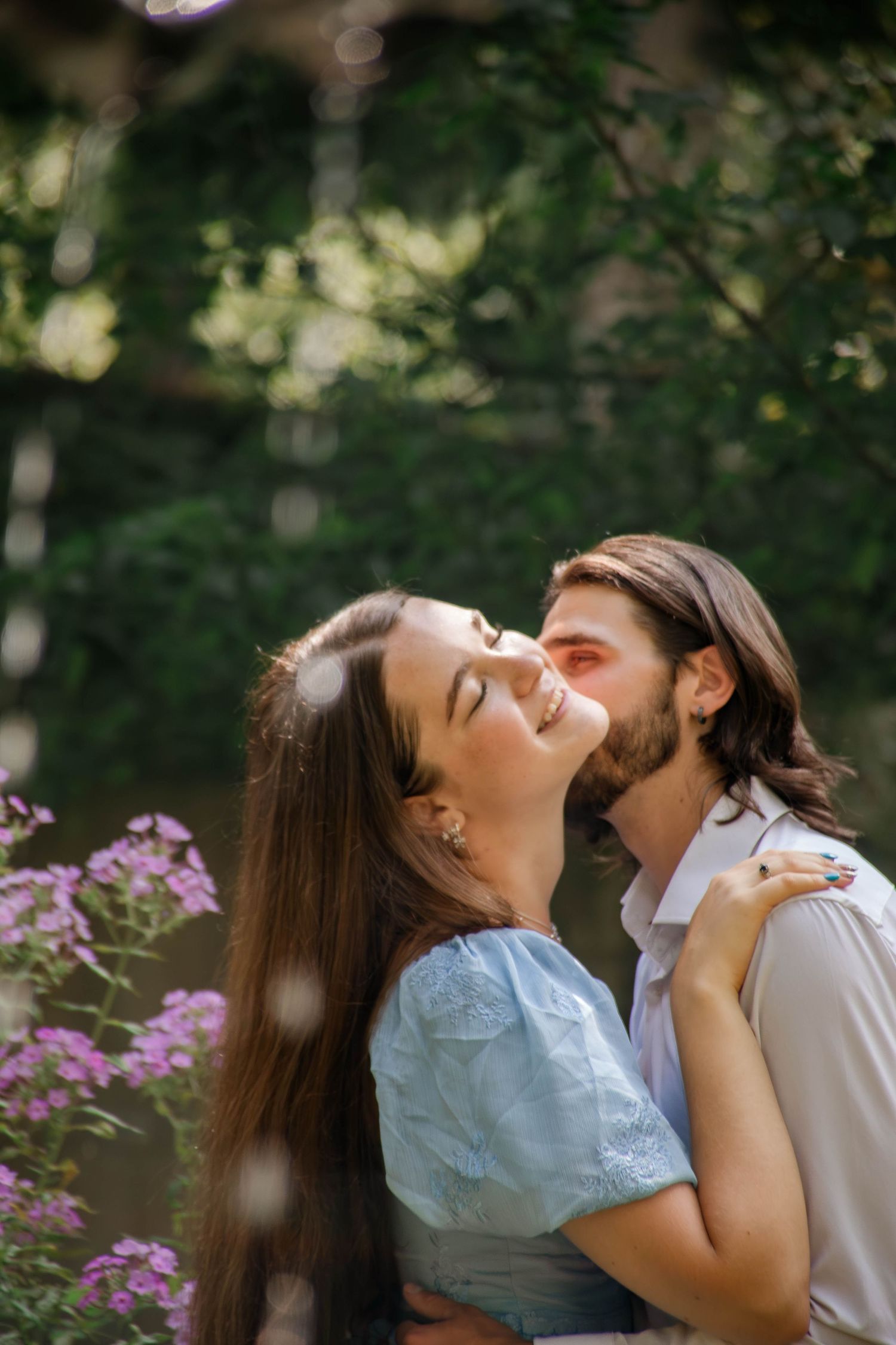 Joyful romantic moment captured in a sunlit garden with purple flowers.