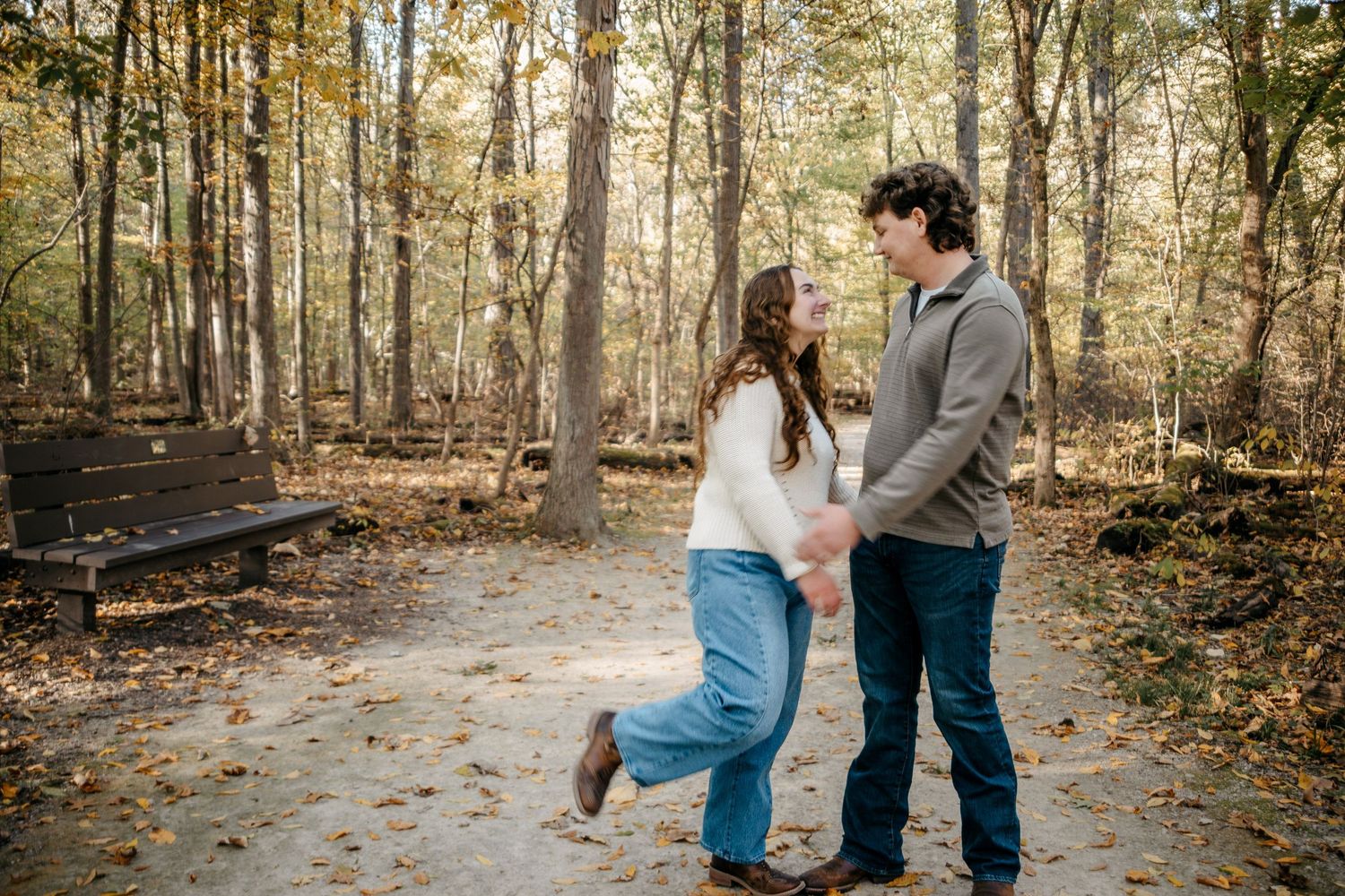 A couple embraces while walking through a leaf-covered forest path in autumn.