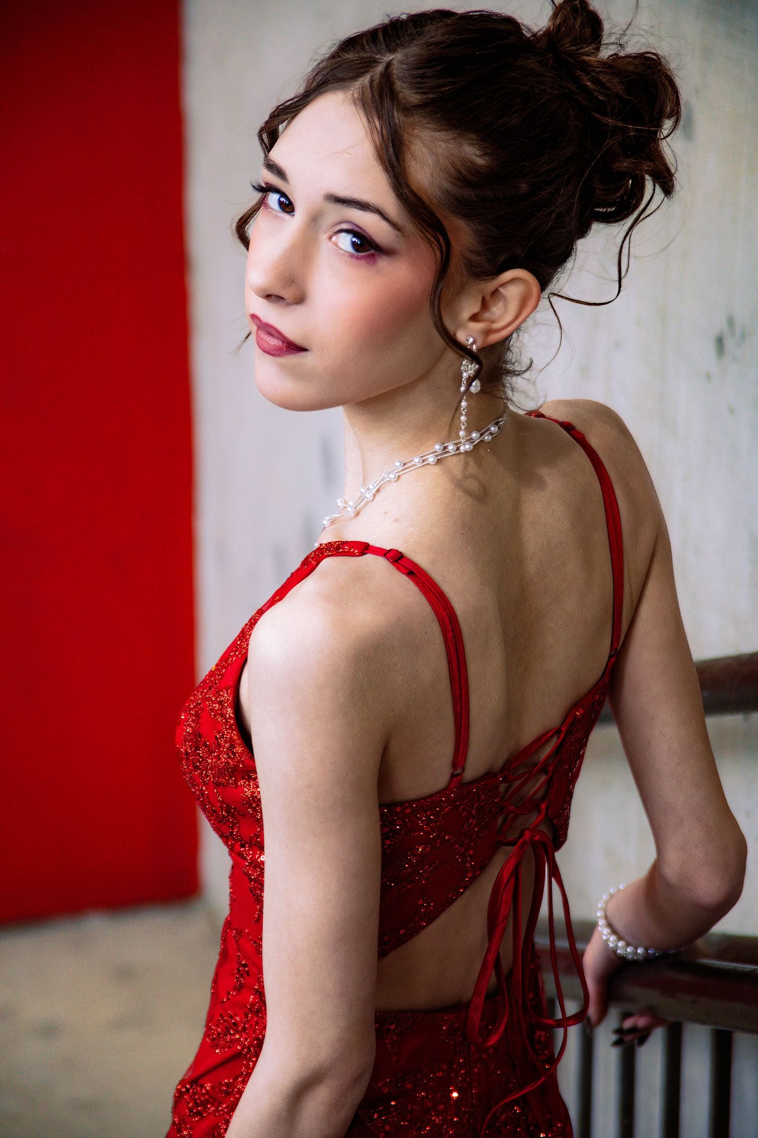A glamorous portrait featuring a sparkly red formal dress and pearl jewelry against a red and white backdrop.