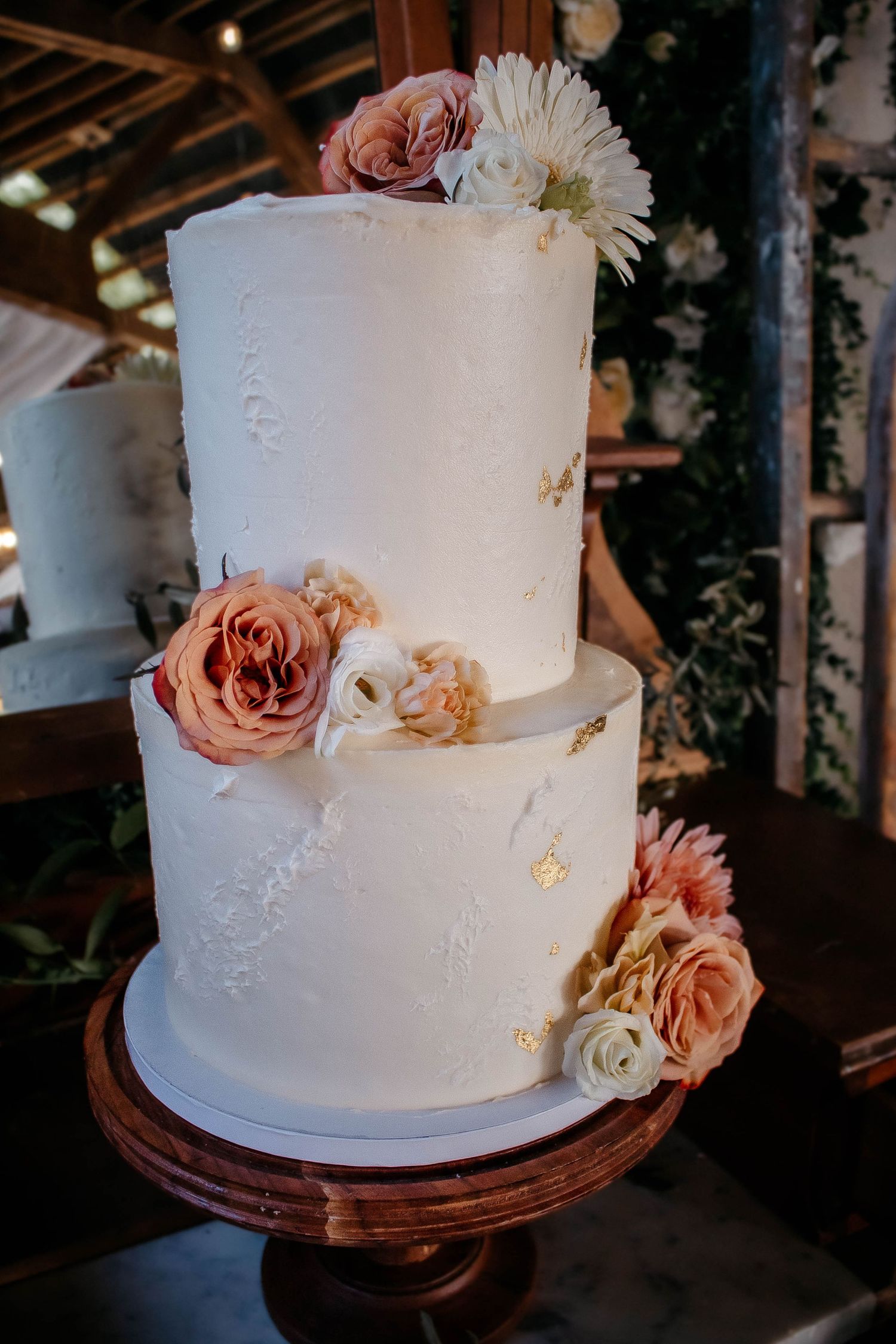 Elegant white wedding cake with delicate lace details and blush pink roses on a wooden cake stand.