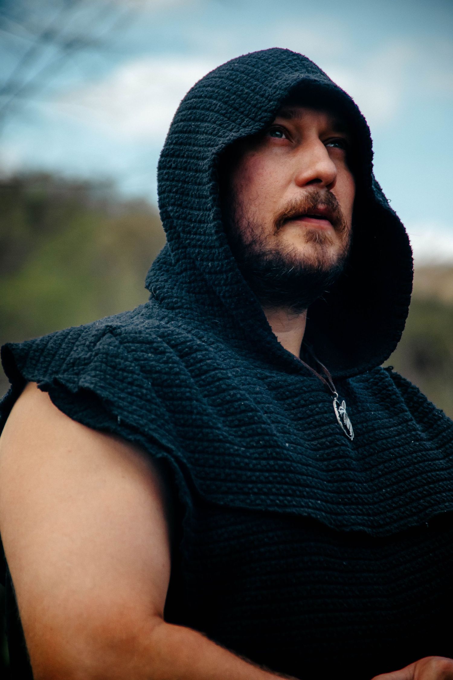 A person wearing a dark knitted hooded cowl gazes into the distance against a blurred background.