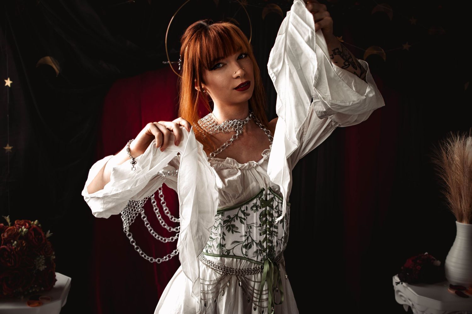 Performer in a flowing white period dress and pearls stands dramatically against a dark theatrical backdrop.