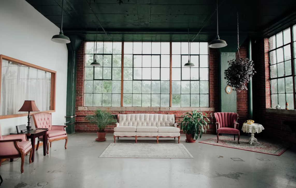 A panoramic view of an industrial-style event space with large windows, hardwood floors, and vintage furniture.