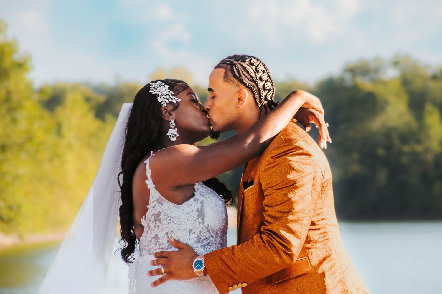 A couple shares a romantic kiss outdoors in formal attire with a bright orange suit and white wedding dress.