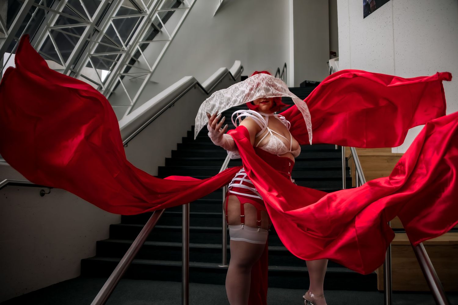 A flowing red cape billows dramatically around a figure on stairs in an artistic indoor photoshoot.