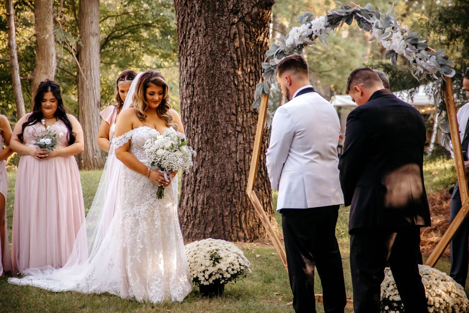 A wedding party gathers outdoors among tall pine trees during a forest ceremony.