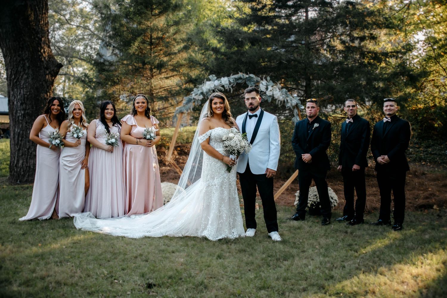 Wedding party stands together outdoors in a natural wooded setting during golden hour lighting.