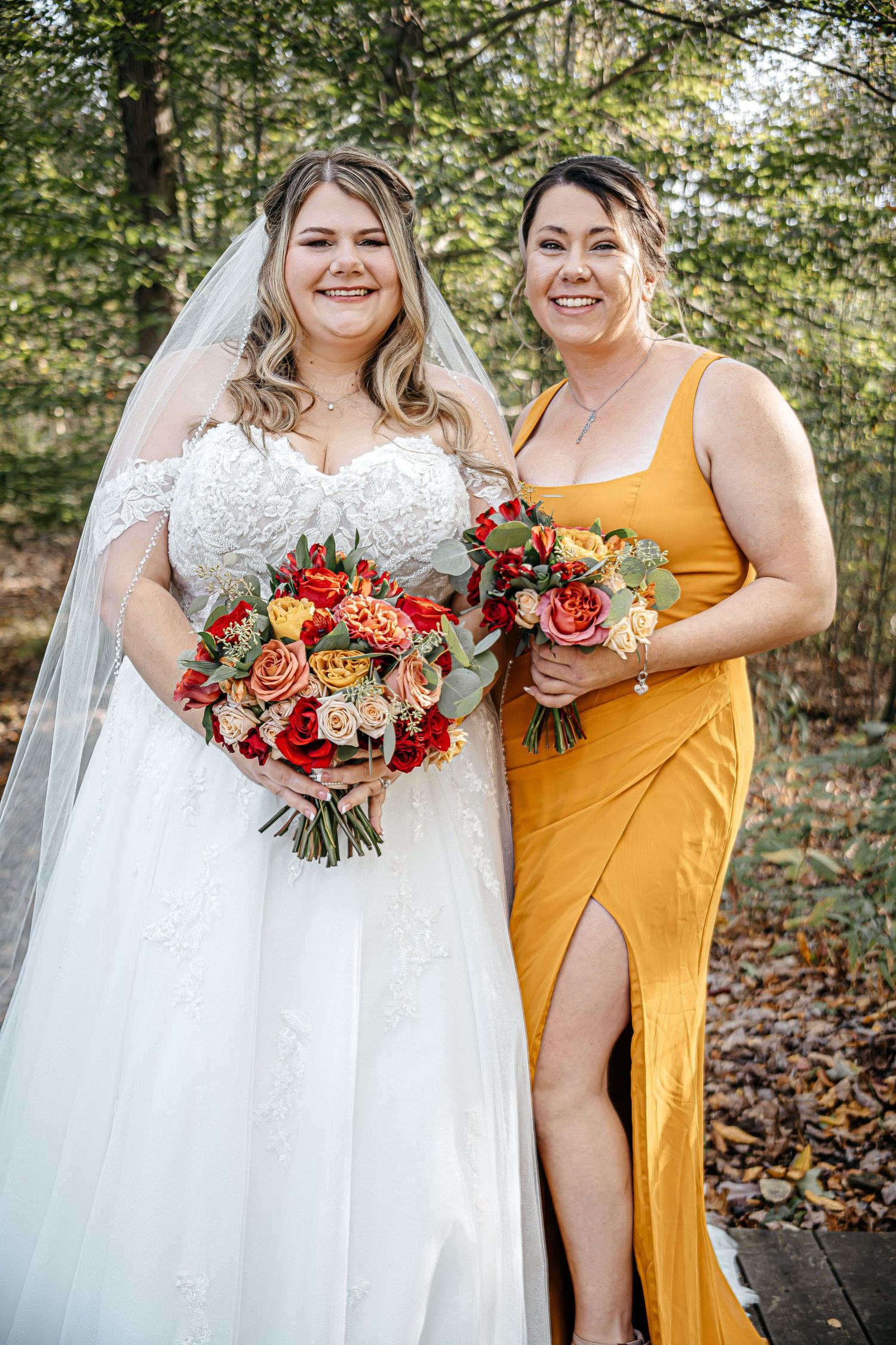 Bridal party members hold vibrant orange and red bouquets while wearing yellow dresses outdoors.