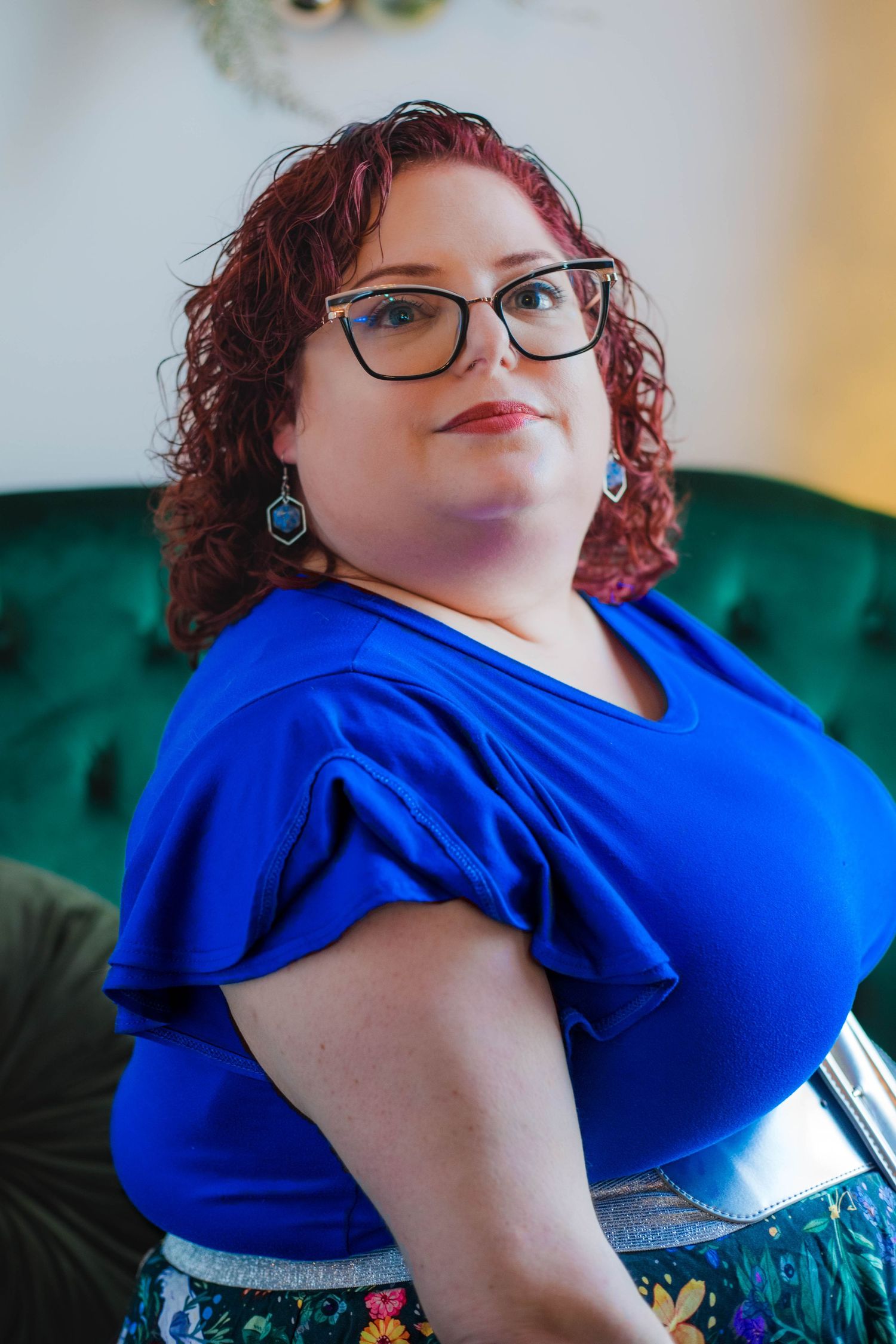Body positive portrait series in a bright blue ruffle top against an emerald green couch.