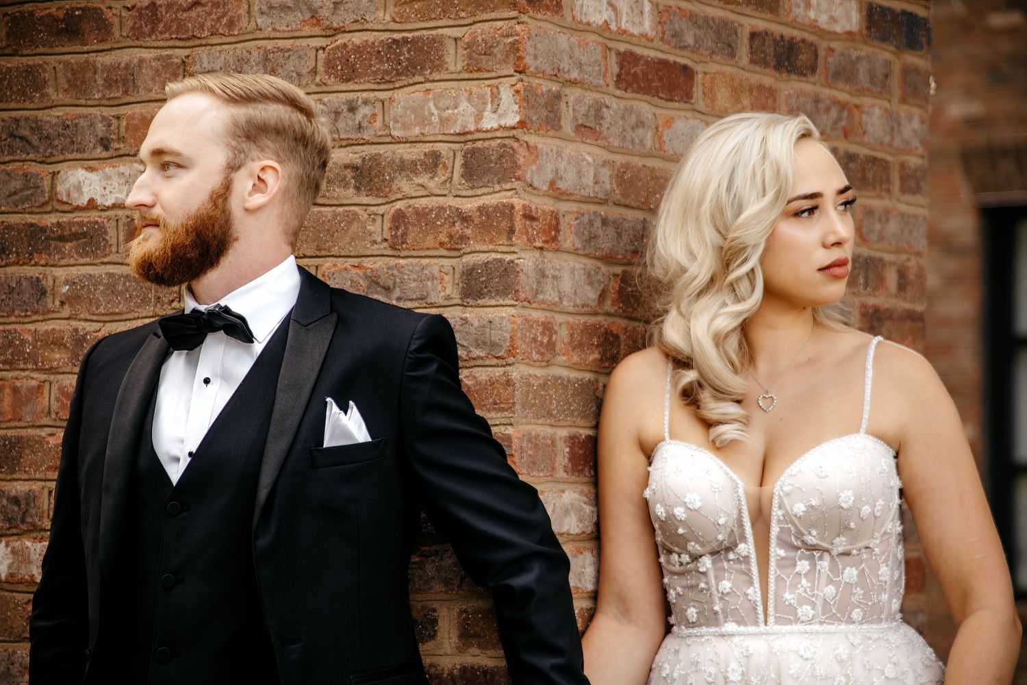 Elegant couple poses against rustic brick wall backdrop during wedding photoshoot.