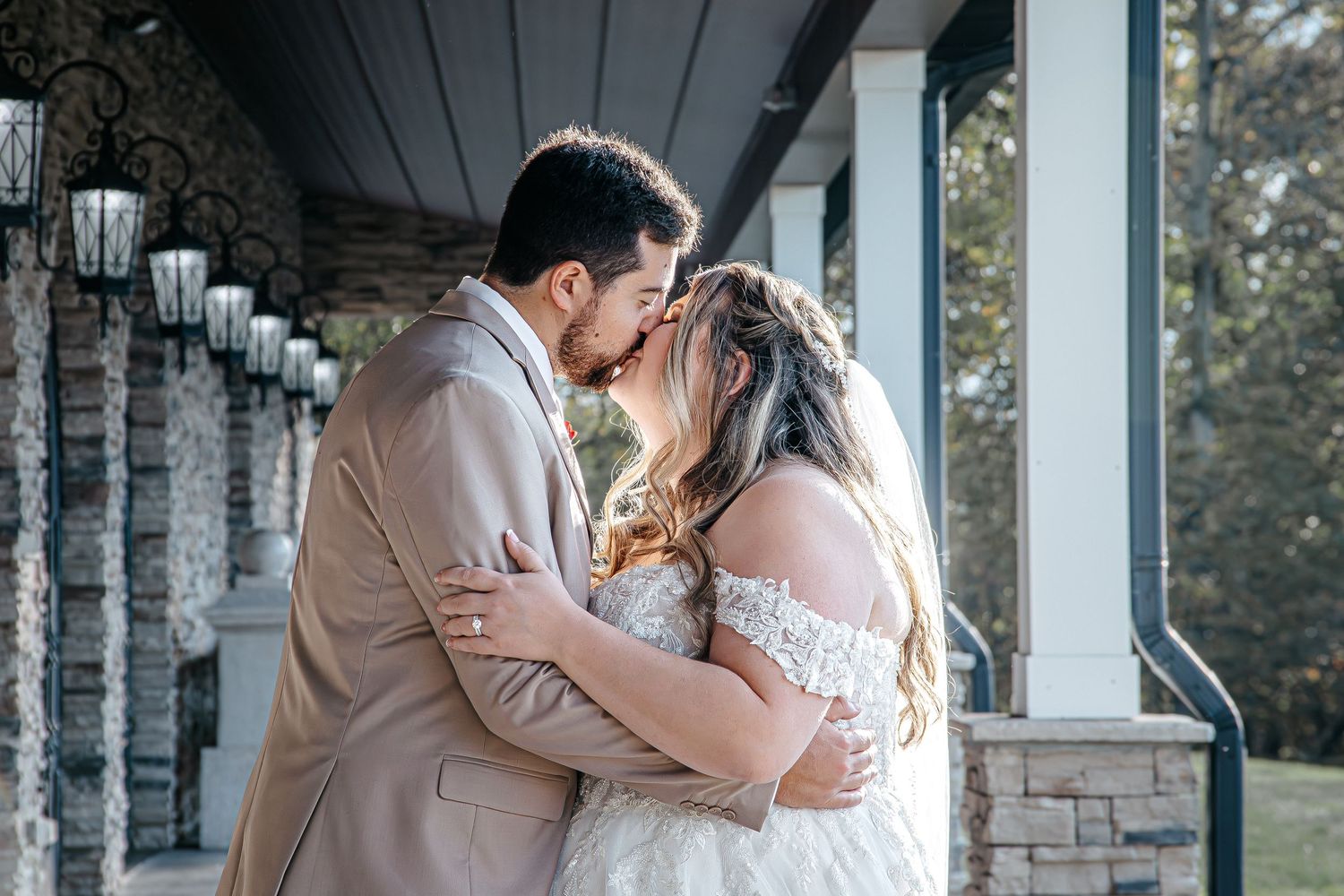 A couple shares a romantic kiss under an elegant stone and white column porch during their wedding day.