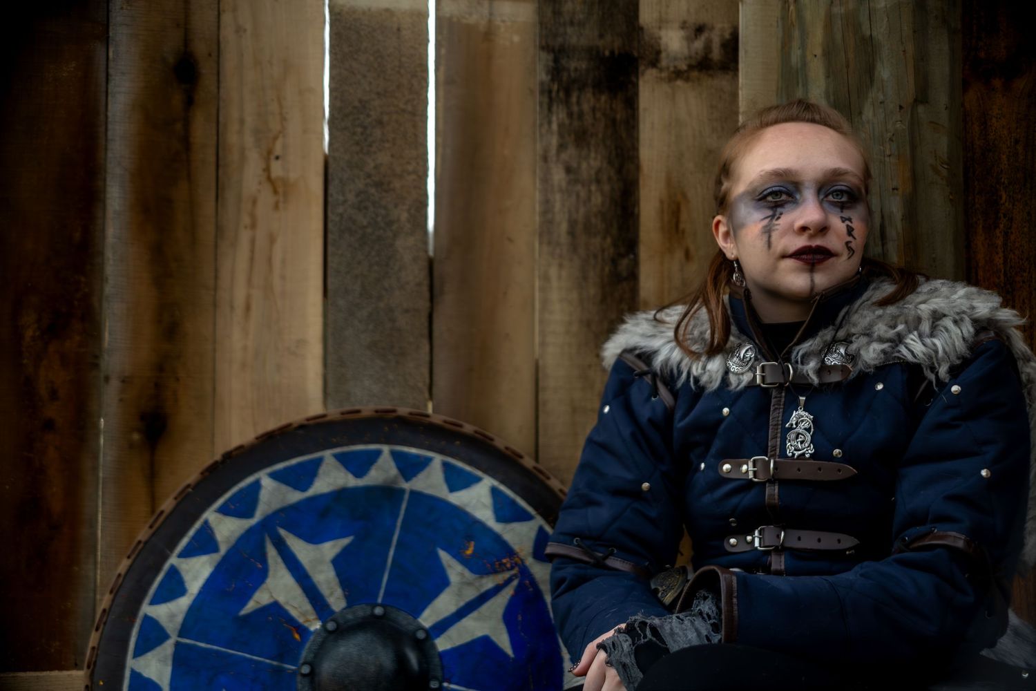 Person wearing a winter coat with fur trim sits against a wooden wall background.