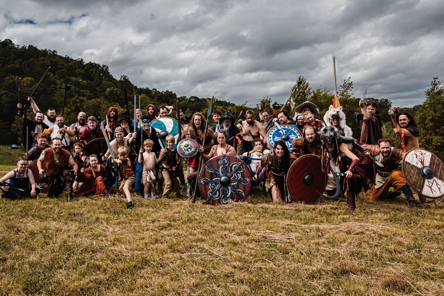A large crowd of festival attendees sits on a grassy hillside under dramatic cloudy skies during an outdoor event.
