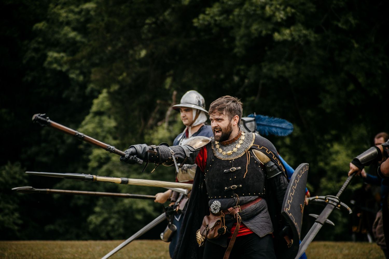 Medieval reenactors in armor wielding spears and shields during an outdoor historical battle demonstration.