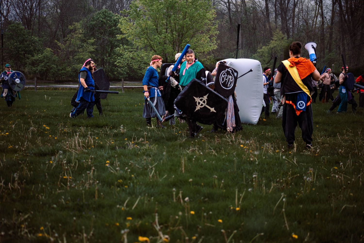 A group of people run through a grassy field with dandelions during an outdoor event.