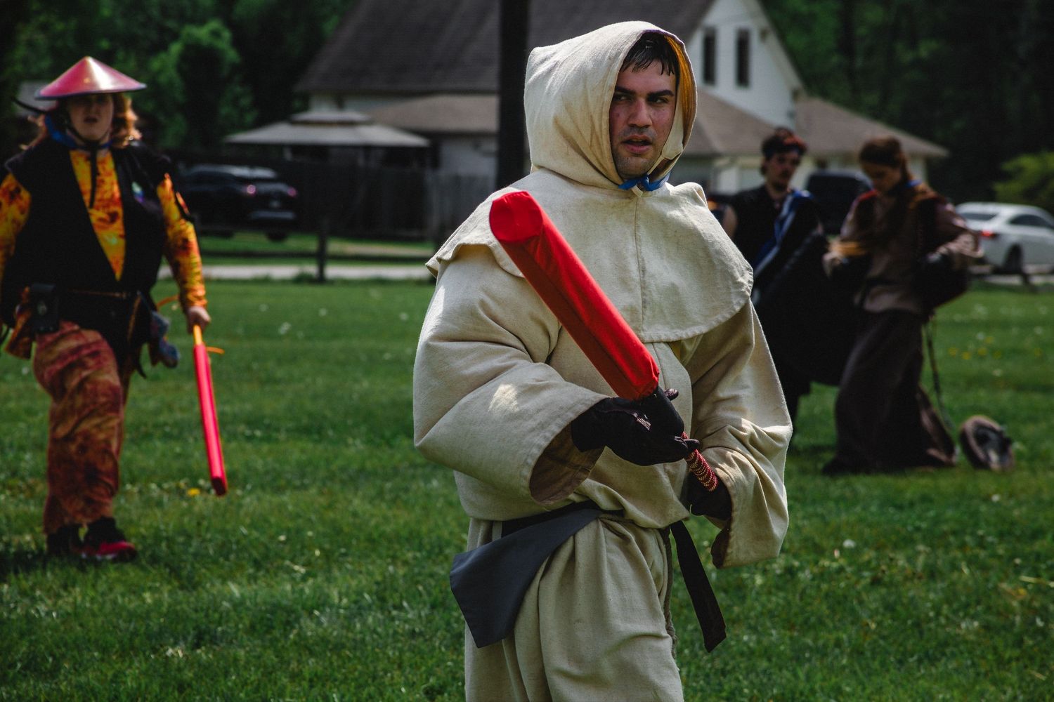 Man in white hooded robe costume holds red foam sword at outdoor medieval LARP battle event.